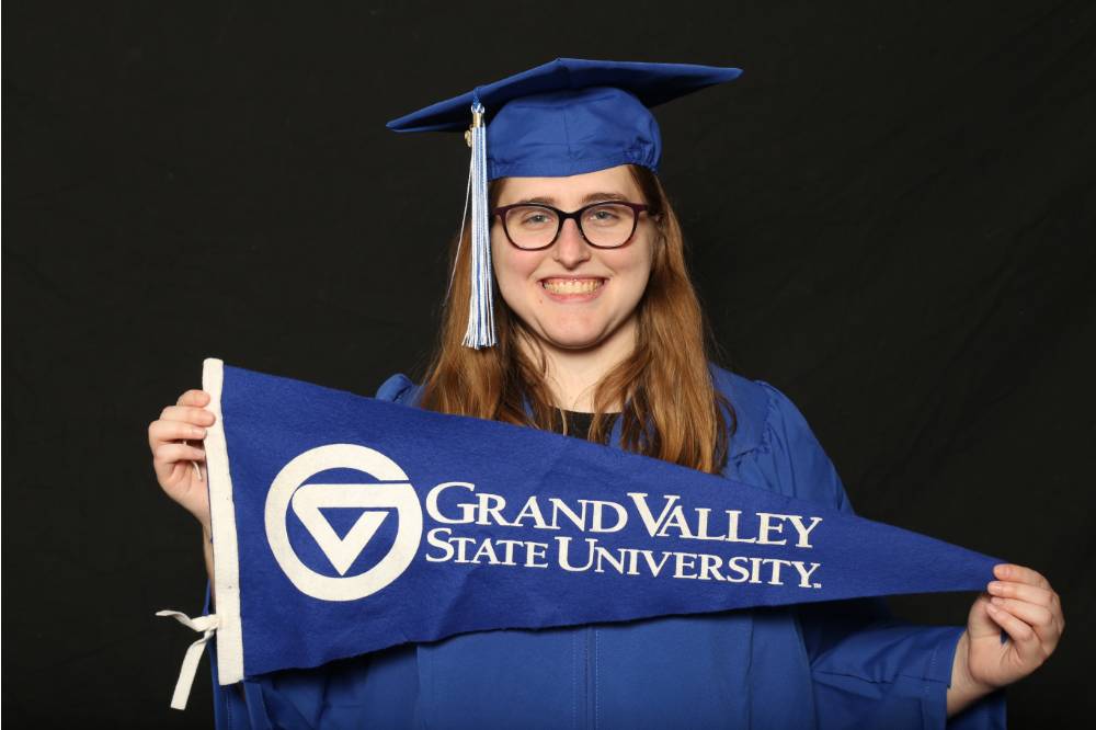 laker in blue cap and gown holding up gvsu flag